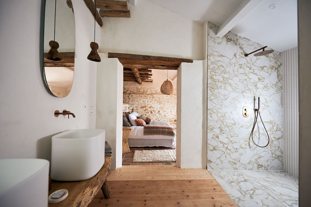 Un baño moderno con un lavabo grande de color blanco, un mueble de tocador de madera, un espejo y una ducha con azulejos de mármol.