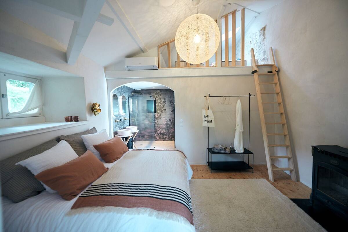 Un dormitorio con una cama grande, un aplique colgante, una escalera y una chimenea.