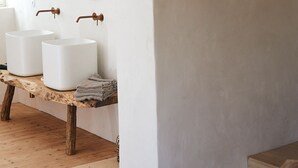 Un baño rústico con vigas de madera, una lámpara de fibra y lavamanos de cerámica blanca.