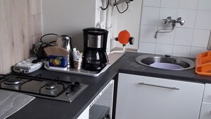 Cocina compacta con estufa a gas, horno, alacenas blancas y un lavamanos.