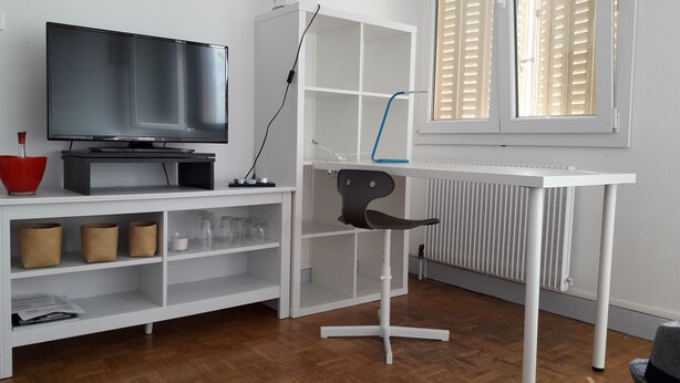 Una sala de estar moderna con televisor de pantalla plana, estanterías blancas, un radiador y una ventana con persianas.