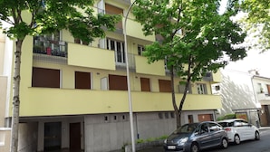 Un edificio residencial de varios pisos con balcones, un estacionamiento y vista a la calle.