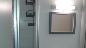 Un baño con cabina de ducha de vidrio, un lavabo con espejo y un estante con artículos de aseo.