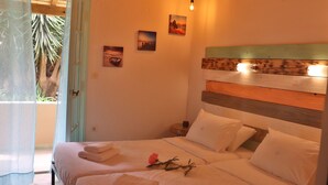 Camera da letto con due letti, una testiera in legno e un balcone con vista su palme.