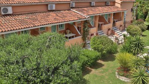 Un edificio a più piani con tetto in tegole rosse, condizionatori d'aria e un giardino con diverse piante e una palma.