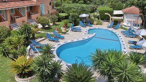 Una piscina circondata da lettini e ombrelloni, con palme e un edificio sullo sfondo.