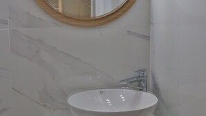 Un bagno con uno specchio rotondo, un lavandino bianco e una mensola in legno.