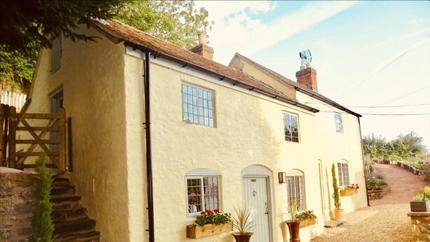 A two-story house with a stone staircase, a front door, and potted plants. - Impeccable 3-bed 17th Century Luxury Cottage (Longhope)