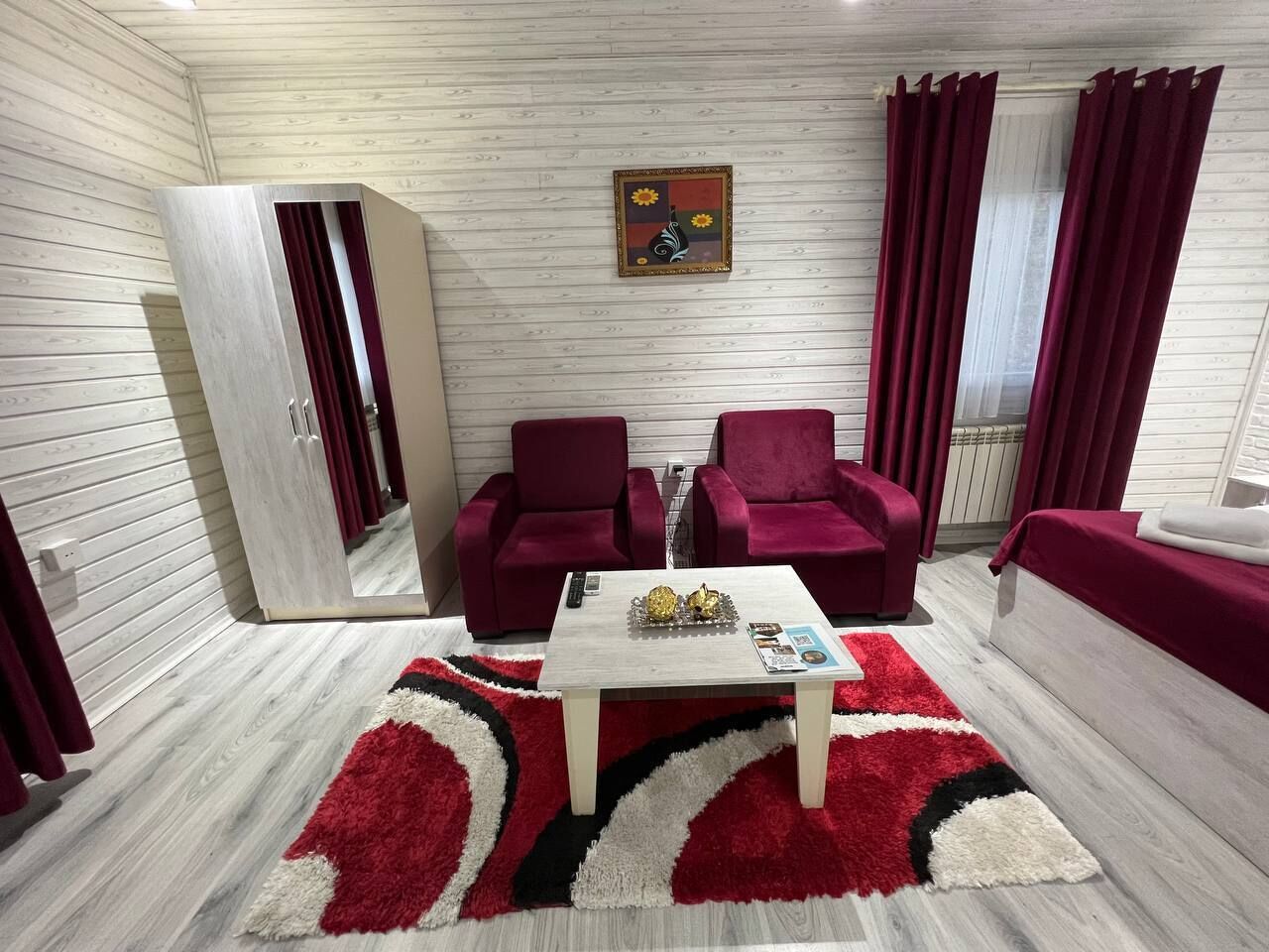 A modern living room with a wooden floor, a white coffee table, two red armchairs, a red sofa, and a wardrobe.