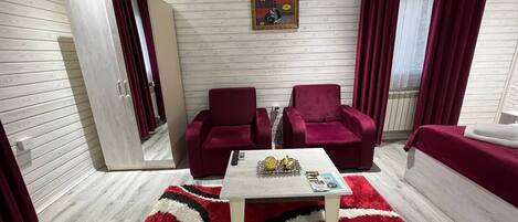 A modern living room with a wooden floor, a white coffee table, two red armchairs, a red sofa, and a wardrobe.