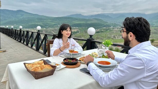 Un tavolo da pranzo con cibo e bevande, una ringhiera e vista su dolci colline.