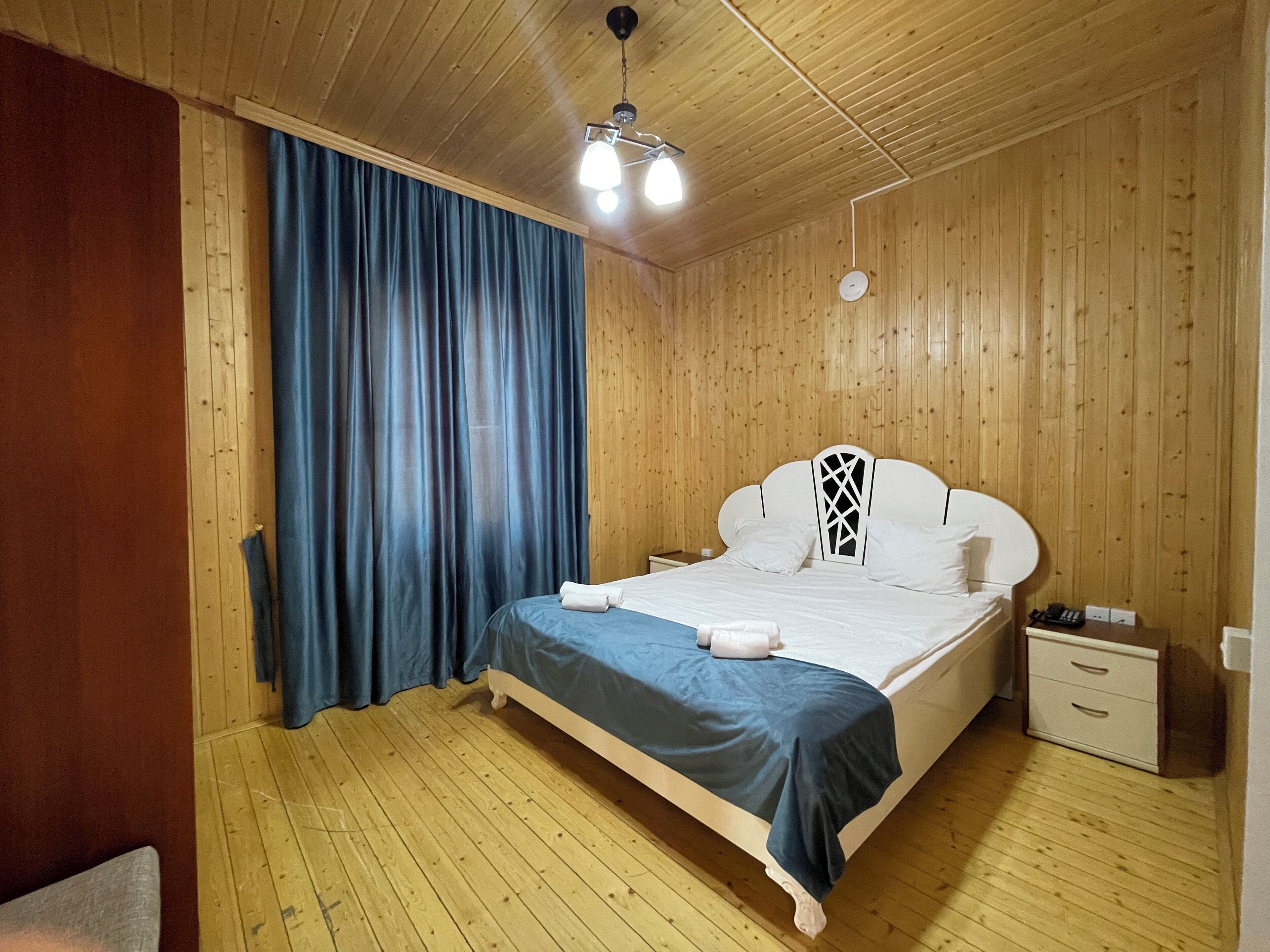 A wooden-paneled room with a bed, a nightstand, and a ceiling light.