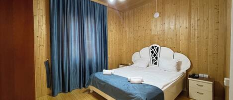 A wooden-paneled room with a bed, a nightstand, and a ceiling light.