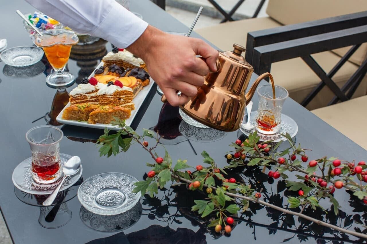 A table set with a variety of desserts, a copper teapot, and glasses of tea.