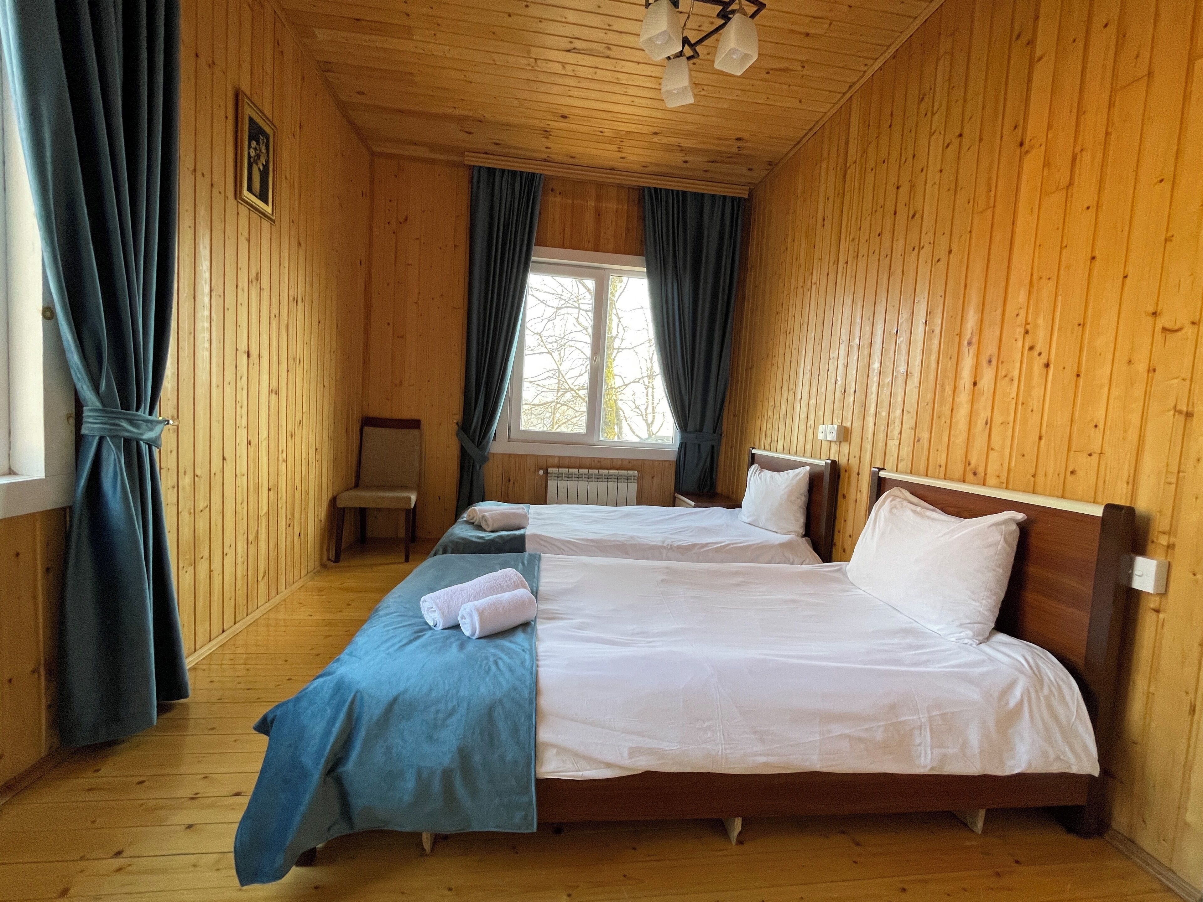 Habitación tipo cabaña de madera con dos camas, una silla, un ventanal y un radiador.