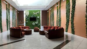 Un'ampia hall con soffitto alto, un'area salotto centrale con divani e tavolino, e pareti decorate da elementi verticali di verde.