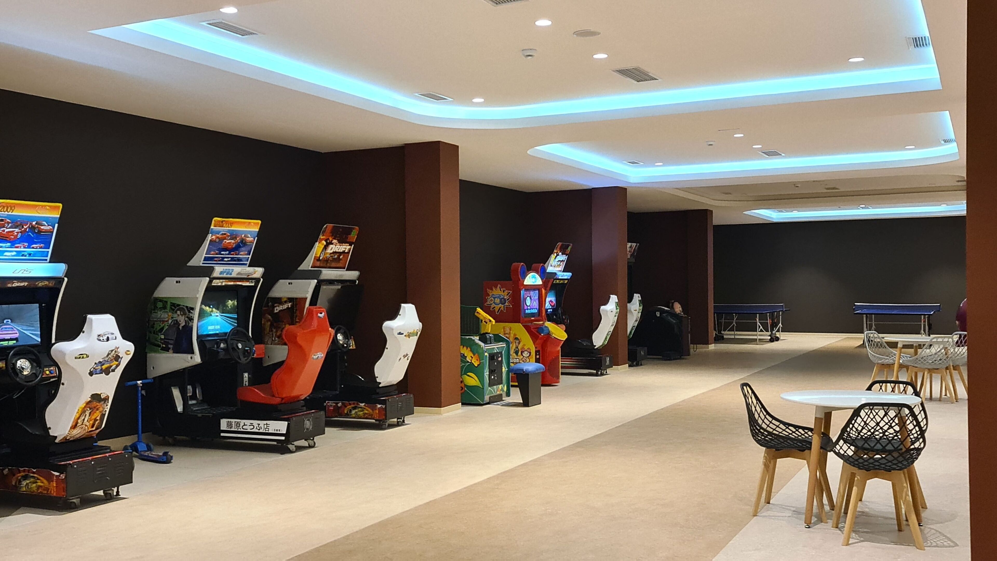 Un'area giochi con diverse macchine arcade, un tavolo da ping pong e un angolo salotto con sedie.