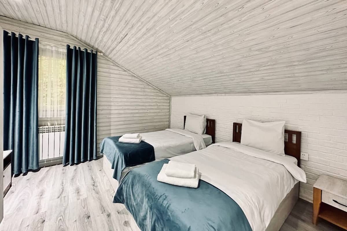 A room with two beds, a window with curtains, and a sloped ceiling.