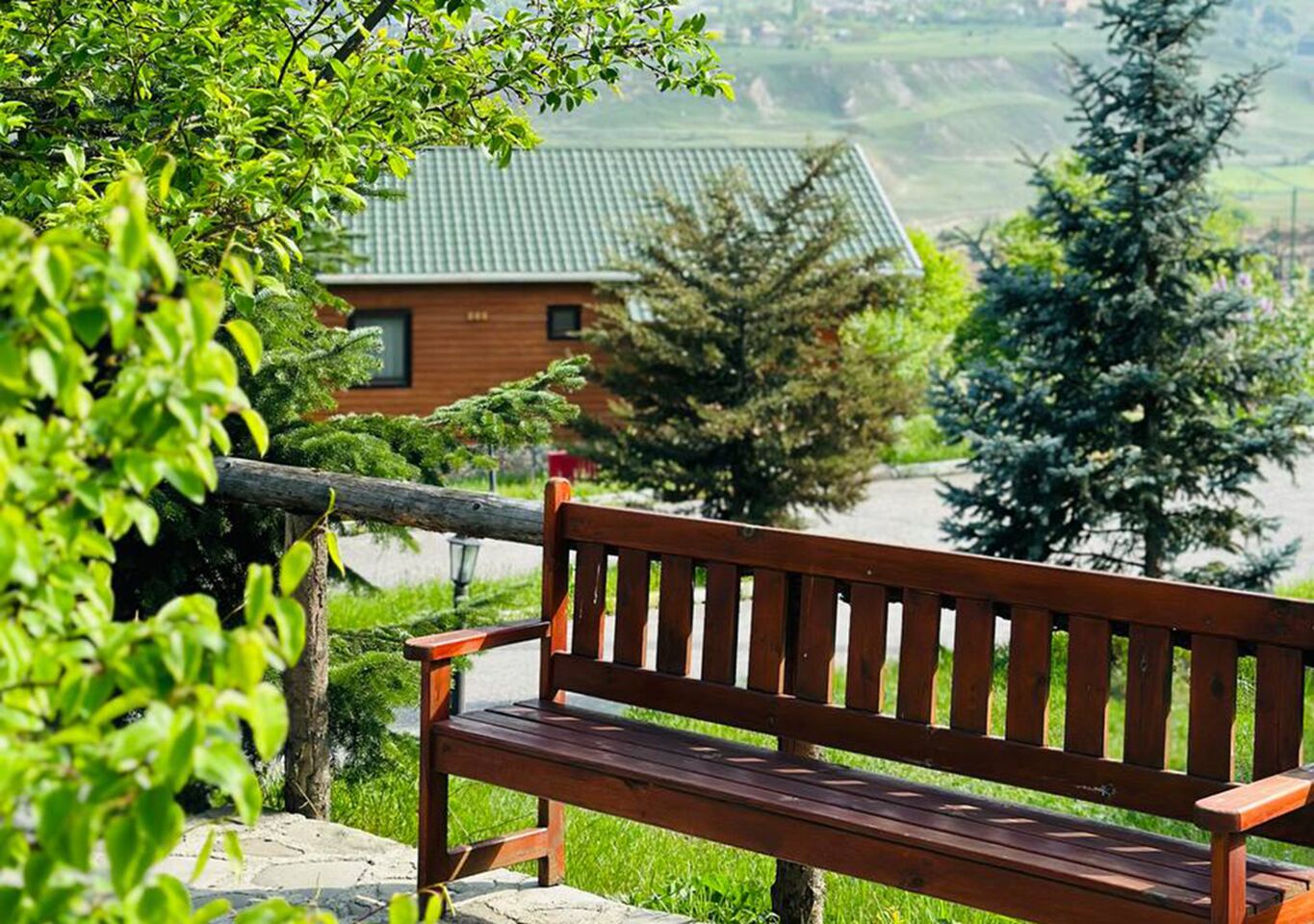 A wooden bench in a lush green setting with a house in the background.