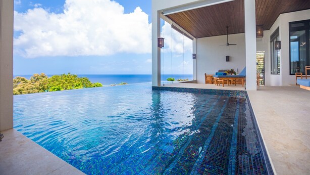 A modern infinity pool with a clear view of the ocean, a wooden ceiling, and a dining area with outdoor seating. - Ocean Pearl 4 Bedroom Home by RedAwning (Roatan)