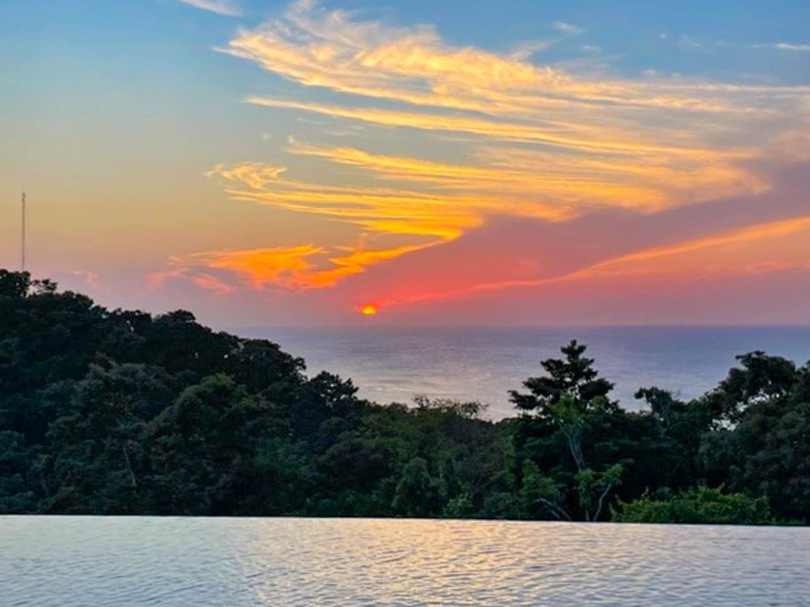 Una vista del atardecer sobre una masa de agua, con un área boscosa al frente.