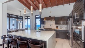 A modern kitchen with a large island, dark cabinetry, stainless steel appliances, and pendant lighting. - Ocean Pearl 4 Bedroom Home by RedAwning (Roatan)