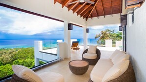 A modern outdoor lounge area with wicker furniture, a ceiling fan, and a view of the ocean. - Ocean Pearl 4 Bedroom Home by RedAwning (Roatan)