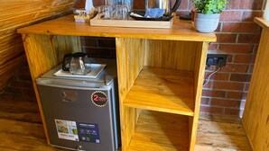 A compact kitchen with a built-in refrigerator, a kettle, and a tray with water bottles and a plant. - Home Villa Eco Boutique (Arusha)