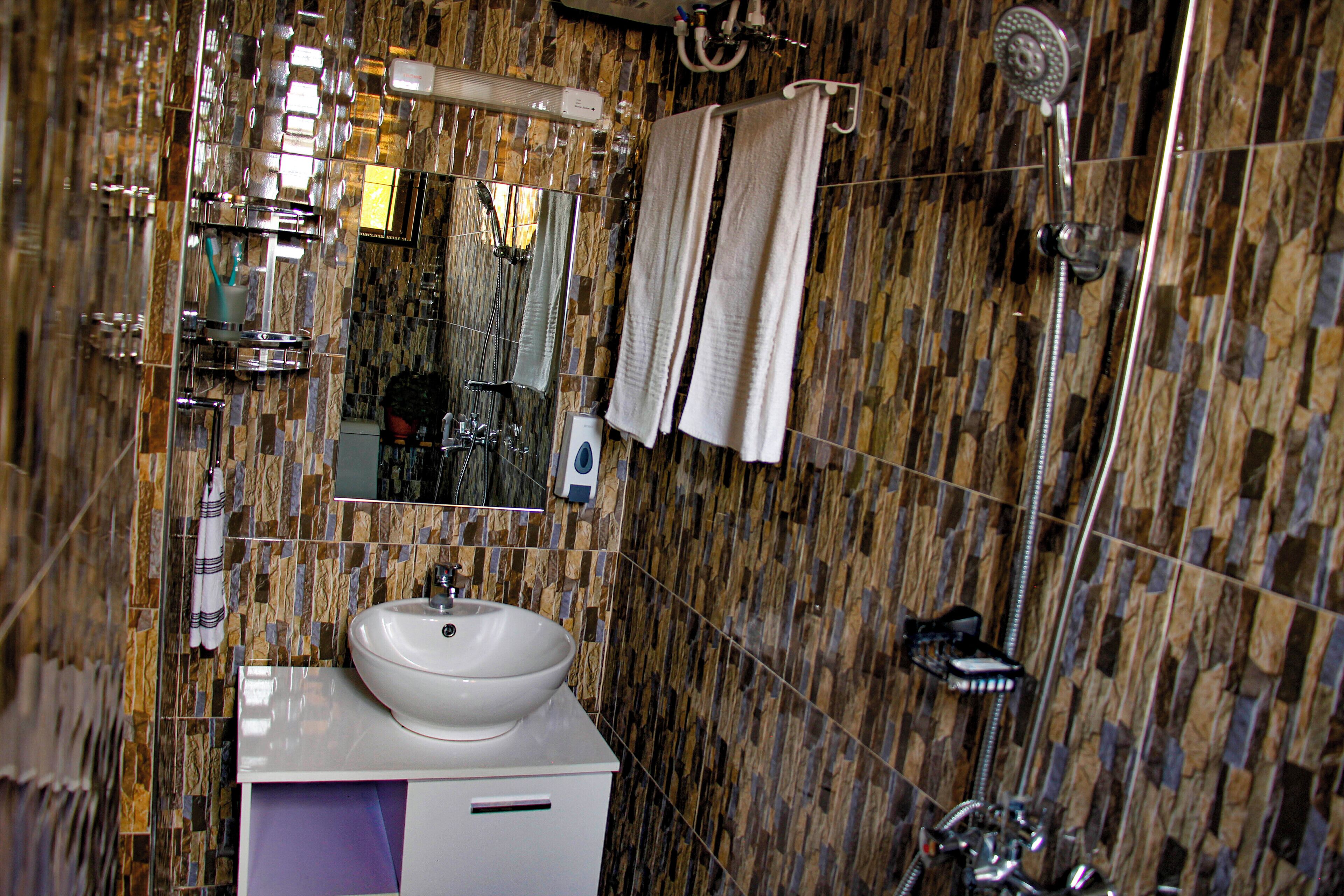 Ein Badezimmer mit Marmorfliesen, einem Waschbecken, einem Spiegel und einer Dusche.