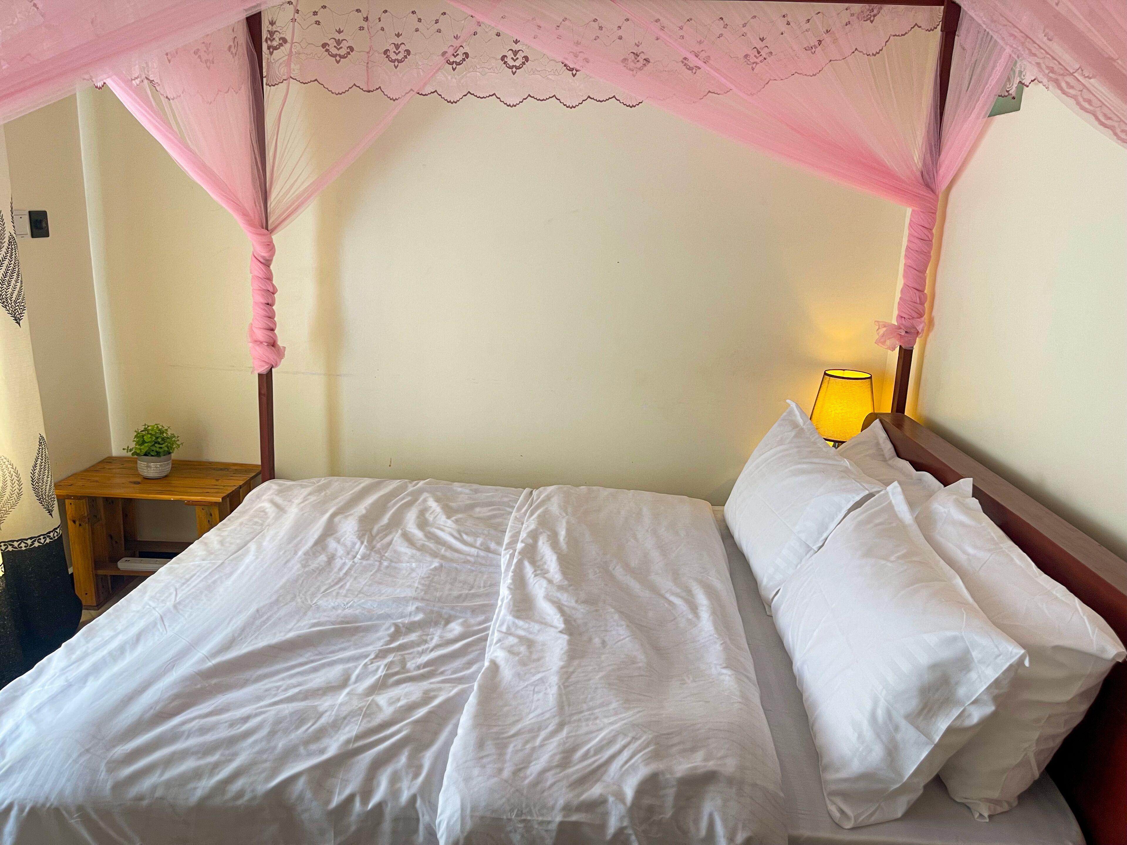 Een bed met witte lakens, een houten nachtkastje met een kleine plant en een bedlamp.