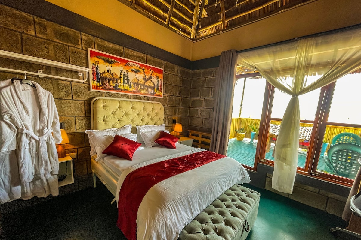 A bedroom with a large bed, a bench, a robe rack, and a painting on the wall.