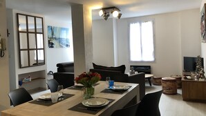 Een eetgedeelte met een houten tafel voor vier personen, omringd door zwarte stoelen. Op tafel staat een vaas met bloemen en aan de muur is een flatscreen televisie bevestigd.