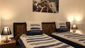 Een hotelkamer met twee bedden, elk met een gestreepte dekbedovertrek en bijpassende kussens. Twee bedlampjes, een houten hoofdbord en een schilderij van een boot aan de muur.
