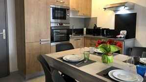 Een moderne keuken met houten kastjes, een ingebouwde oven, magnetron en koffieapparaat. Er staat een eettafel gedekt met borden, glazen en een vaas met bloemen.