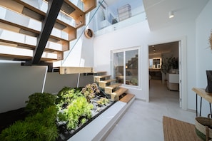 A modern interior with a glass staircase, a small garden, and a view into the living area.