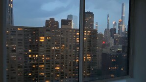 A view of a cityscape through a window, featuring multiple high-rise buildings with illuminated windows. - NYC Luxury 3bed/3 bath Westside Manhattan  (New York)