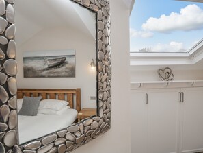 Ein Schlafzimmer mit einem spiegelnden Steinrahmen, einem Bett mit weißer Bettwäsche, einem Gemälde eines Bootes an der Wand und einem Oberlicht über einem weißen Kleiderschrank.