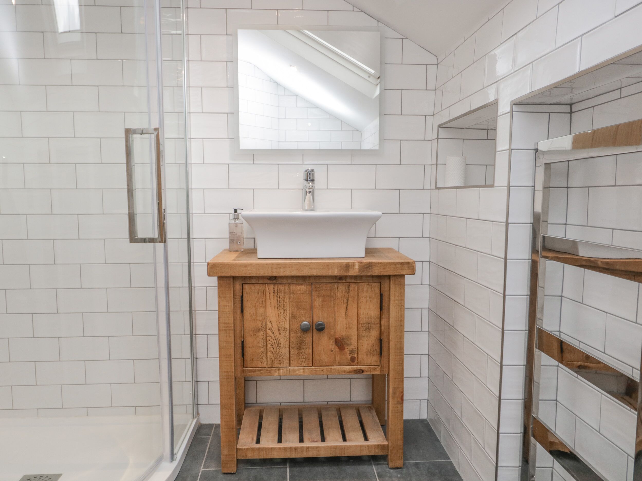 Ein Badezimmer mit einem weißen Waschbecken, einer Holz-Kommode und einem Spiegel darüber.