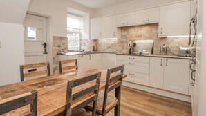 Una cocina moderna con armarios blancos, una mesa de comedor de madera y un ventanal que proporciona luz natural.
