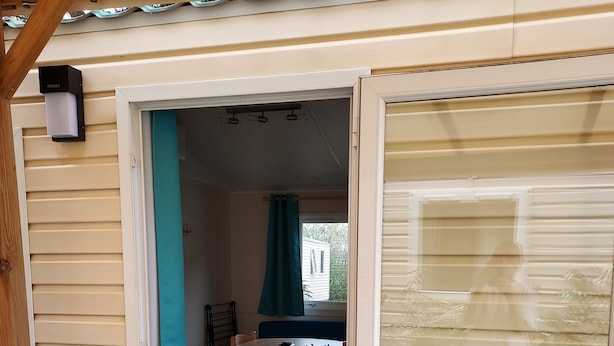 Una terraza de madera que lleva a un cuarto con puerta de vidrio corrediza, una mesita y una silla.
