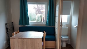 Pequeña habitación con una mesa de madera y un banco, una ventana con cortinas, un inodoro y un radiador.
