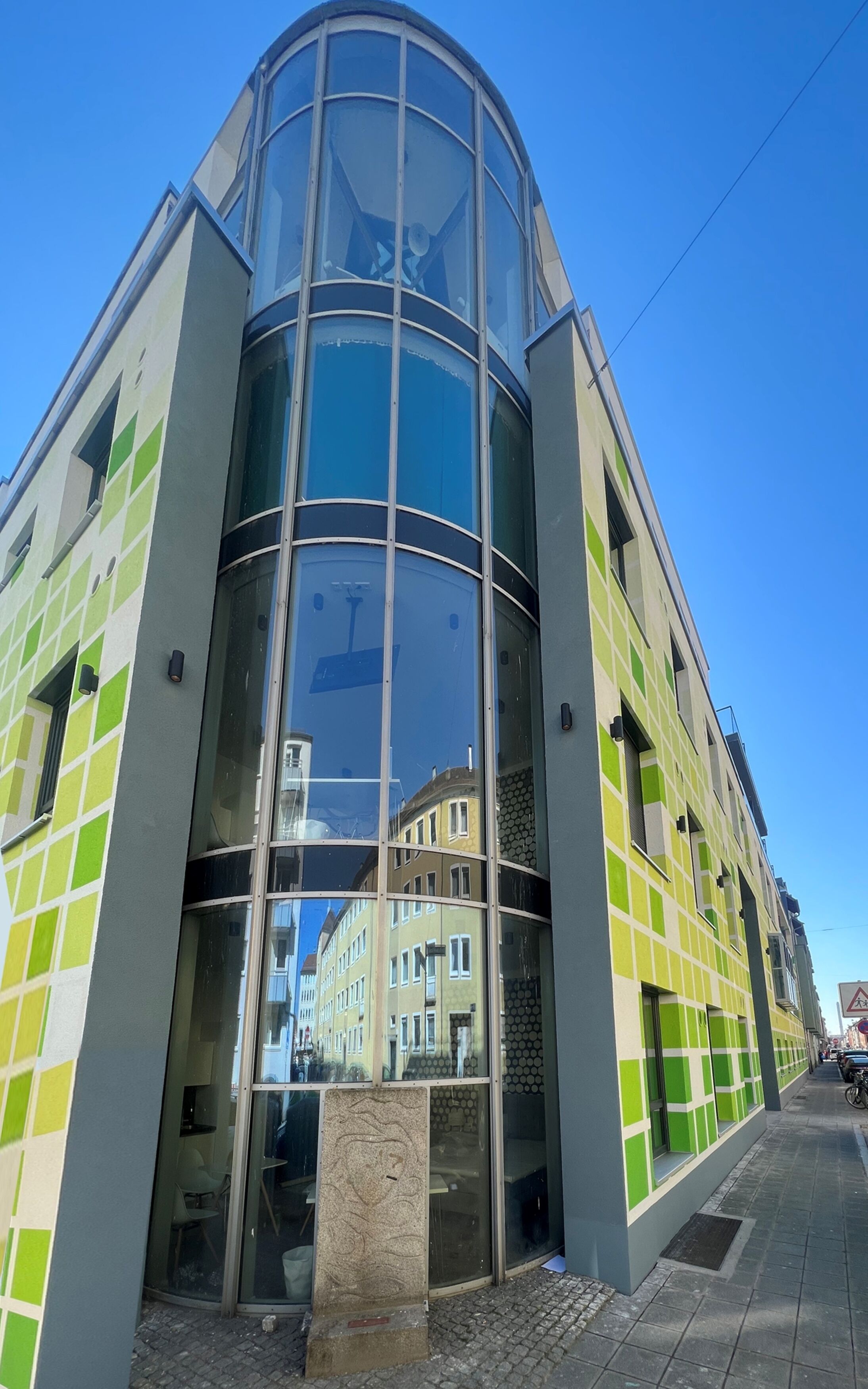 A modern building with a curved glass facade and green-tiled exterior.