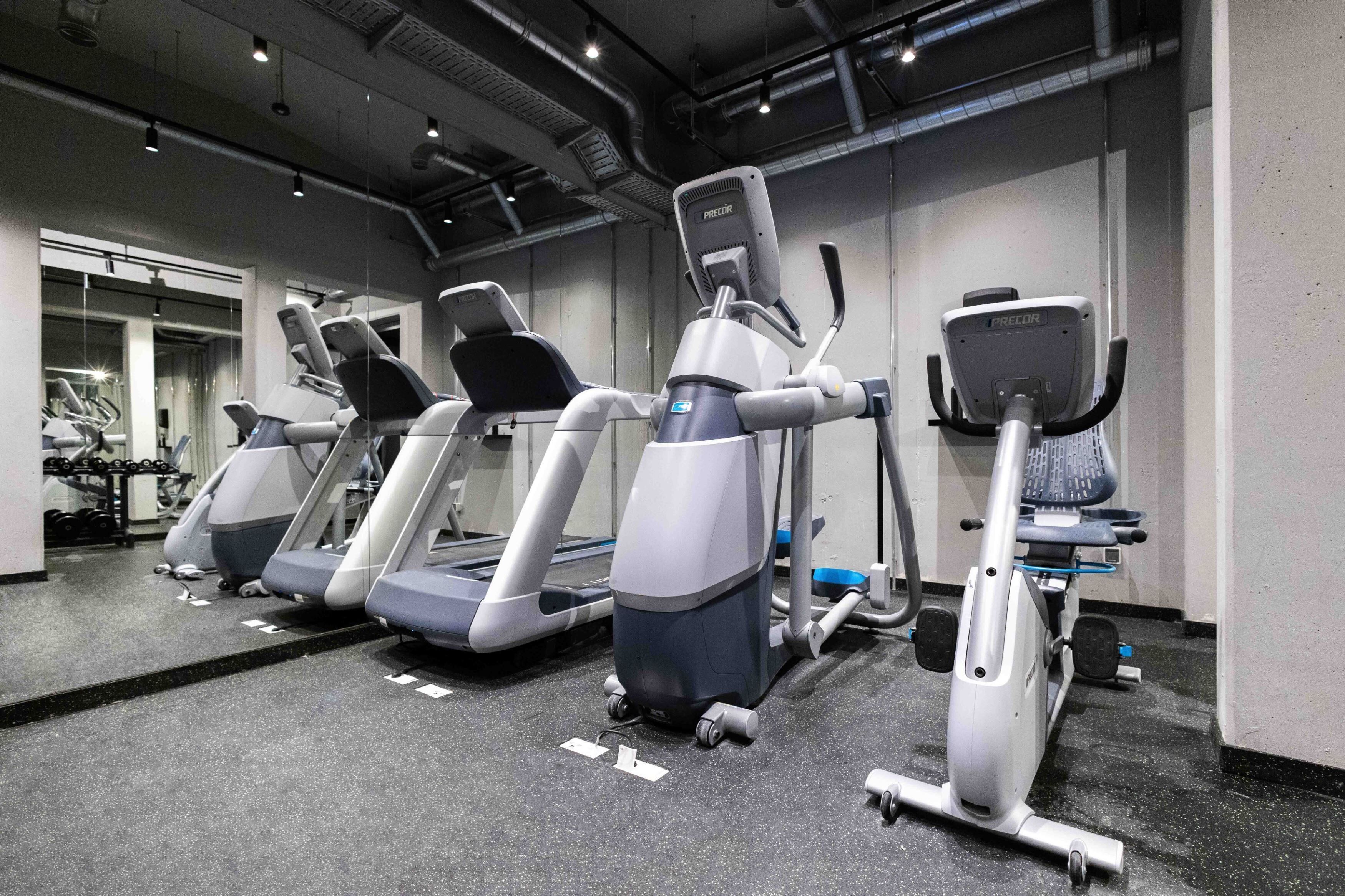 Ein Fitnessstudio mit Laufbändern, Crosstrainern und einer Spiegelwand.
