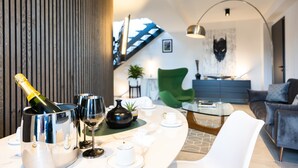 A modern living room with a curved white table, a green armchair, and a sofa. A bottle of champagne and wine glasses are on the table. - Penthouse at Eco Smart Apartments (Nuremberg)