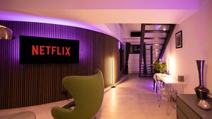 A modern interior with a Netflix sign, a green chair, a desk, and a staircase. - Penthouse at Eco Smart Apartments (Nuremberg)