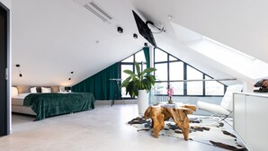 A modern loft bedroom with a sloped ceiling, a large window, a sofa, a coffee table, and a white cabinet. - Penthouse at Eco Smart Apartments (Nuremberg)