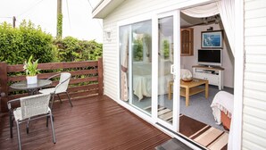 Eine gemütliche Außenterrasse mit Tisch und Stühlen, eine Glastür zum Raum mit Fernseher und Esstisch.