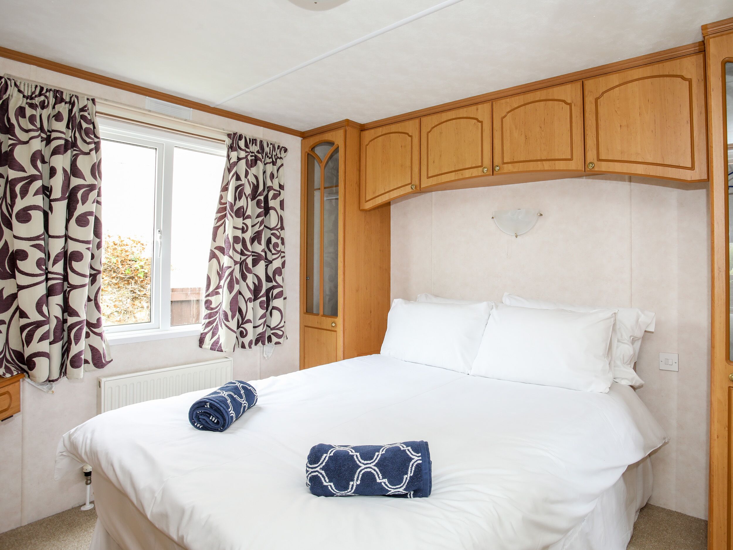 A bedroom with a bed, curtains, wooden cabinets, and a radiator.