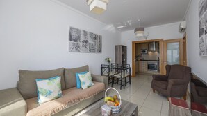 Un salon moderne avec un canapé, une table basse et un coin repas avec des chaises. On peut apercevoir la cuisine à travers une porte ouverte.
