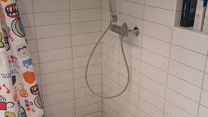 A small, tiled bathroom with a shower, toilet, and a shelf with toiletries. - 2-bedroom apartment in central Oslo. Located right next to Løren subway (Oslo)